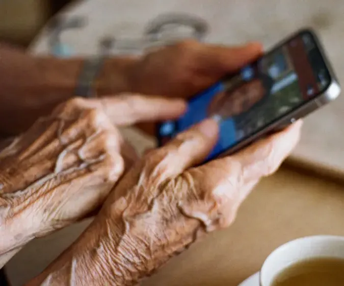 Gros plan sur des mains tenant un smartphone affichant un appel vidéo, avec une tasse de thé posée à proximité